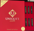 A luxury perfume discovery set in a red box, with the lid standing open next to the box interior showing several slim black perfume strips with gold lettering.
